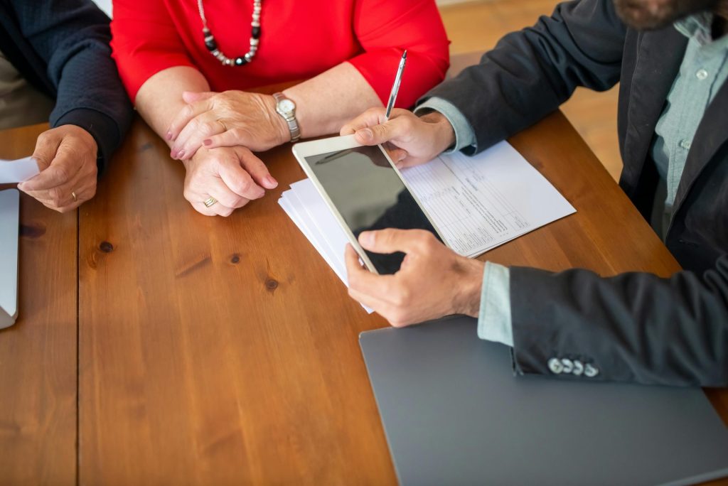 Réunion d'affaires autour d'une table en bois, avec un consultant qui examine des documents et utilise une tablette numérique.